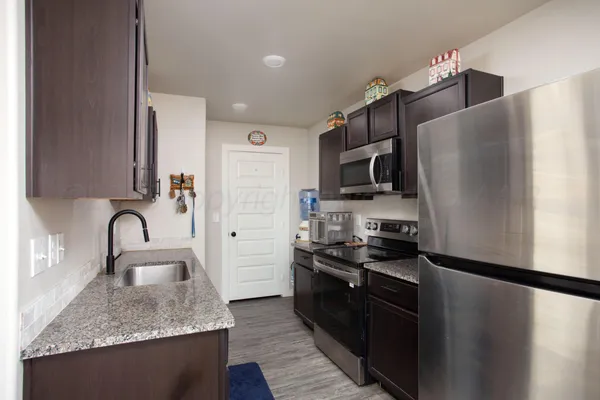 a kitchen with stainless steel appliances granite countertop a sink dishwasher a refrigerator and a stove with wooden floor