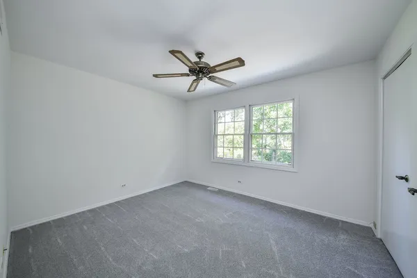 an empty room with a chandelier fan and windows