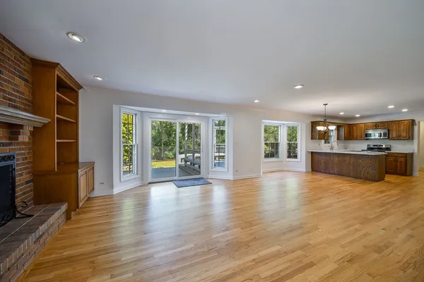 a view of an empty room with wooden floor and a kitchen