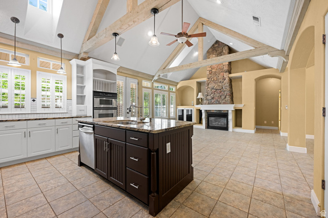20 Valley Road Leeds, UT 84746 - Photo 10 of 57 Vaulted ceiling with exposed wood beams highlights this open-concept kitchen and living area, featuring a stone-clad fireplace, built-in shelving, and a kitchen island with a granite countertop