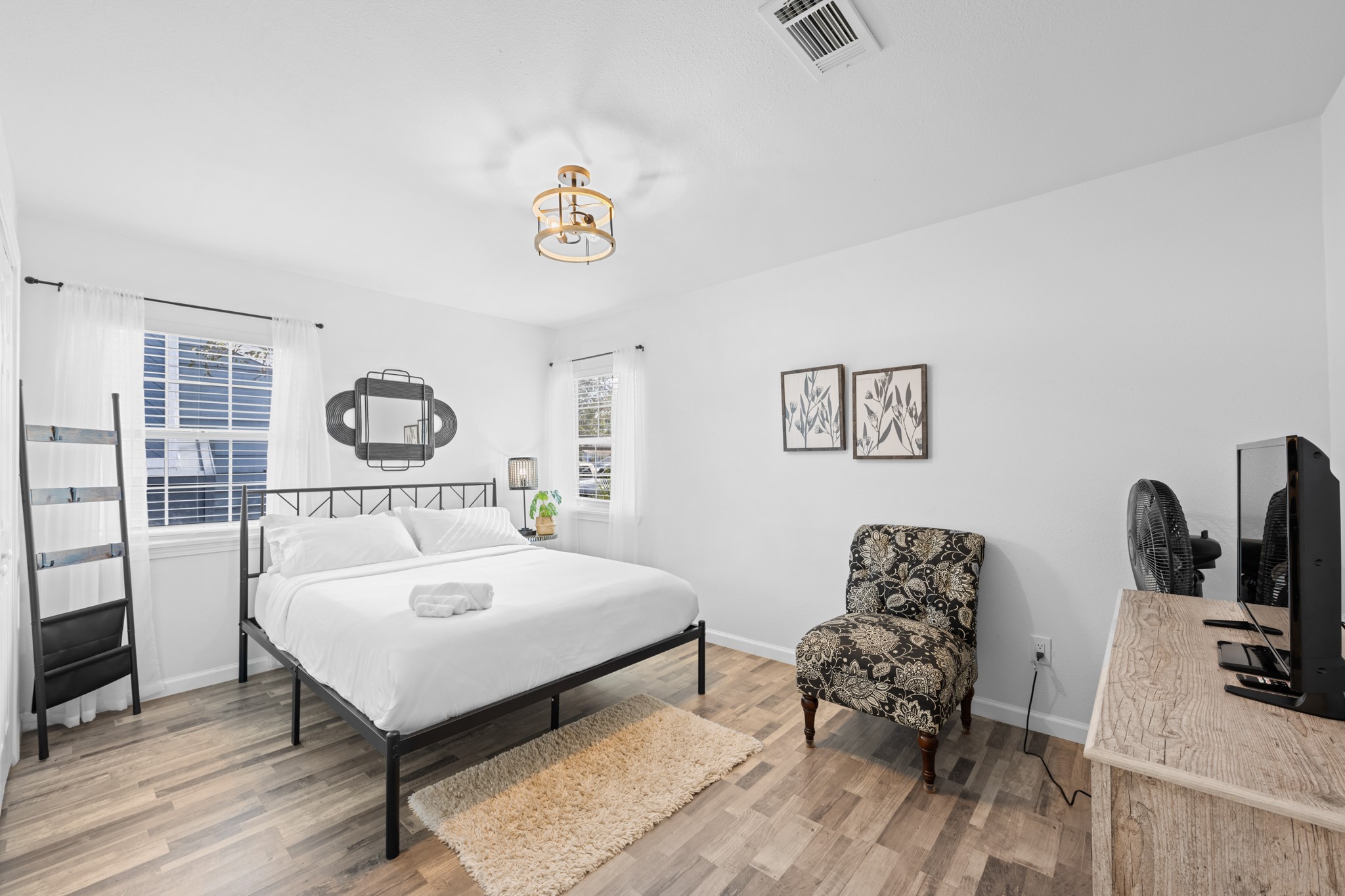 729 Kyle Angleton, TX 77515 - Photo 26 of 36 Bright and airy bedroom with modern decor, featuring a comfortable bed, large windows with ample natural light, a patterned chair, and a wooden dresser.