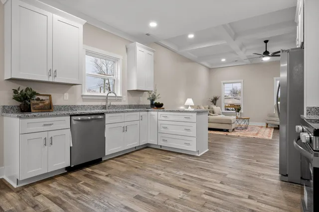 a kitchen with stainless steel appliances kitchen island granite countertop a stove a sink a refrigerator and white cabinets with wooden floor