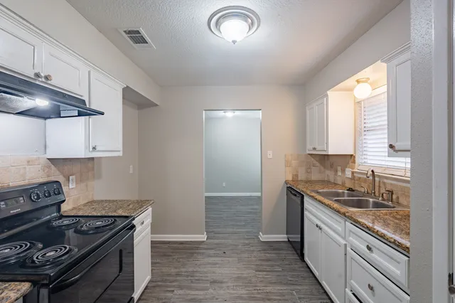 a kitchen with granite countertop stainless steel appliances white cabinets granite counter tops and a wooden floors