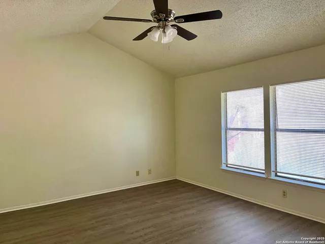 an empty room with wooden floor fan and windows