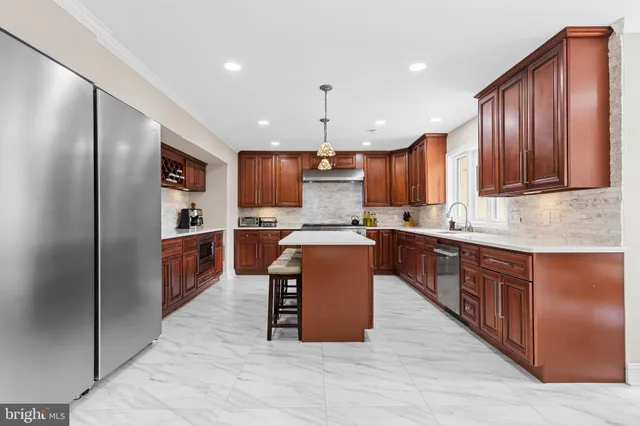 a large kitchen with stainless steel appliances granite countertop a refrigerator a sink dishwasher a oven and a dining table with wooden floor