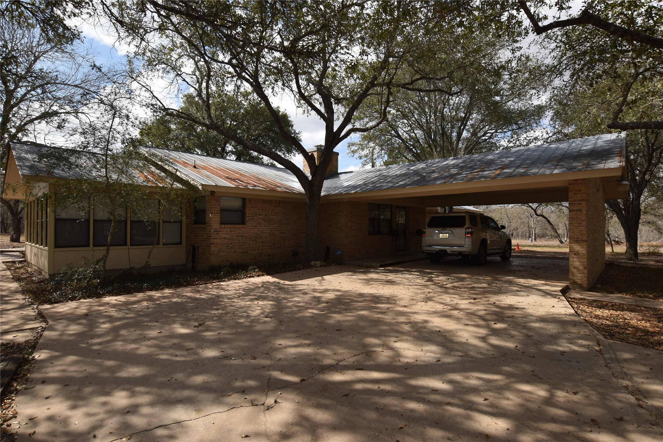687 Fm 812 Road Red Rock, TX 78662 - Photo 5 of 40 View of home's exterior featuring a sunroom, concrete driveway, brick siding, a carport. and newly shingled roof on 3/17/2026.