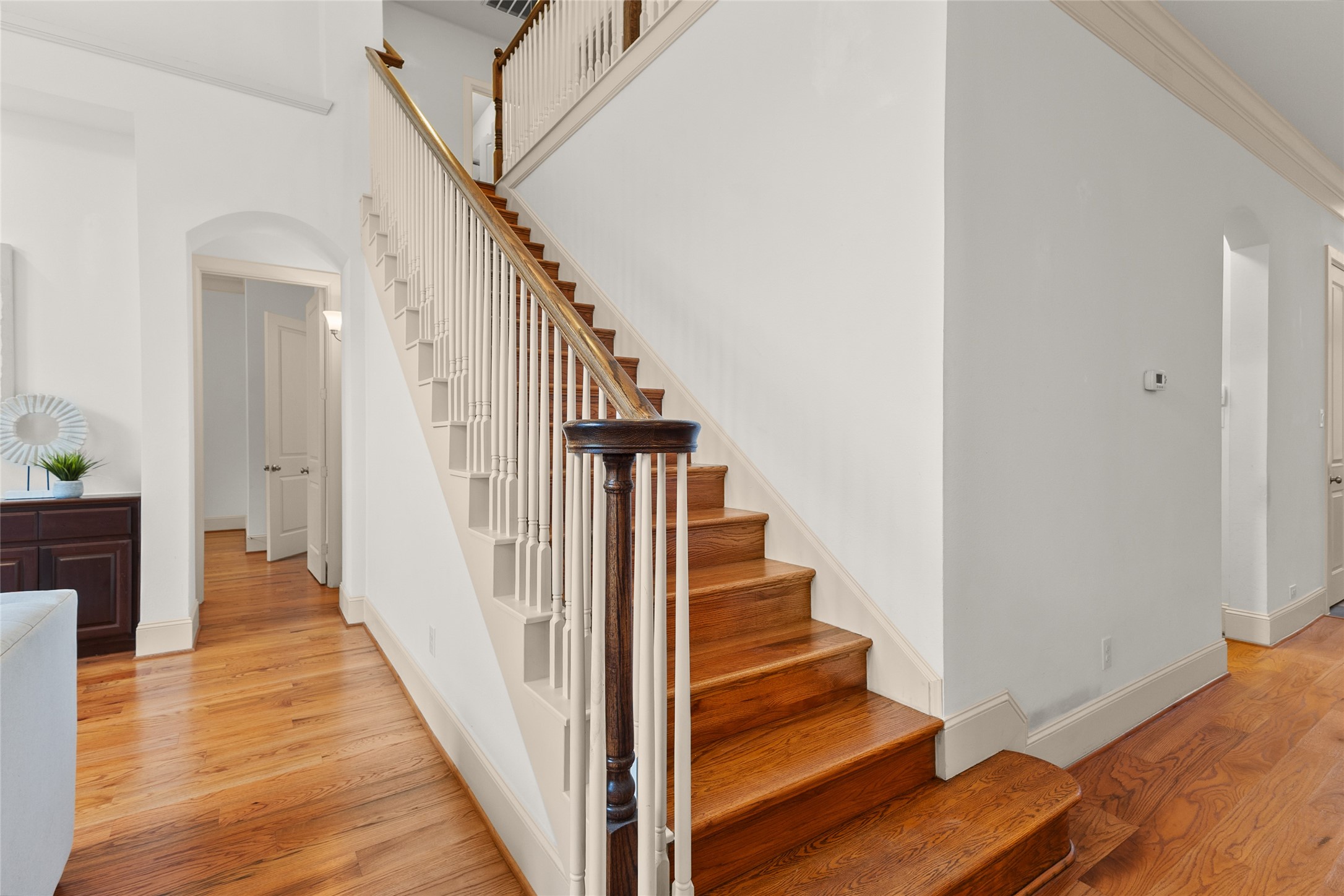 3302 Rochdale Street Houston, TX 77025 - Photo 30 of 50 This elegant staircase offers a striking centerpiece to the home, with rich wood treads, classic turned balusters, and a warm handrail leading up to the second floor. Hardwood floors carry through the surrounding hallway, connecting easily to the arched doorway and living spaces nearby.