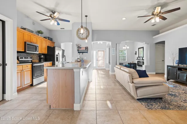 a large living room with stainless steel appliances kitchen island granite countertop couches a fireplace and a flat screen tv