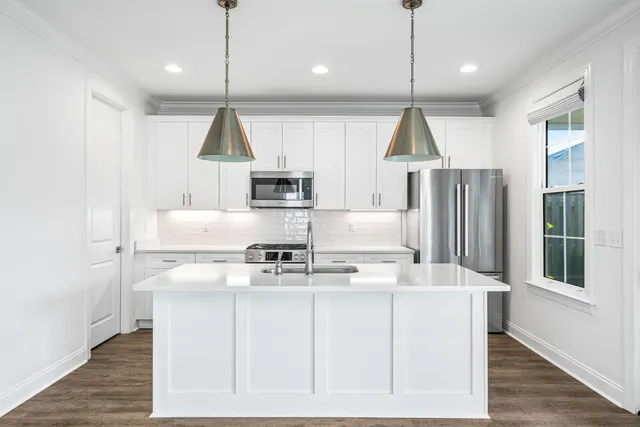 a kitchen with kitchen island stainless steel appliances a stove a refrigerator white cabinets and wooden floor