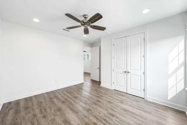 an empty room with wooden floor fan and windows