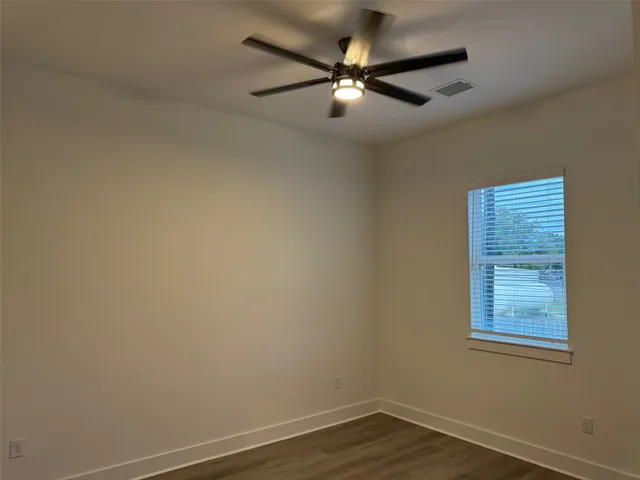 an empty room with wooden floor fan and windows