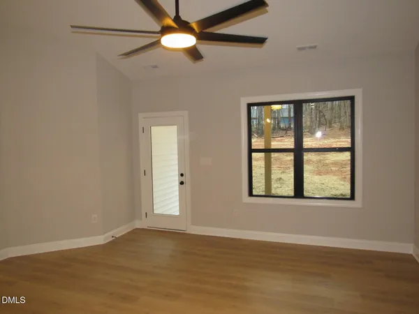 an empty room with wooden floor fan and windows