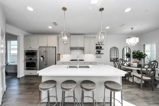 a kitchen with stainless steel appliances a stove a sink a refrigerator a dining table and chairs with wooden floor