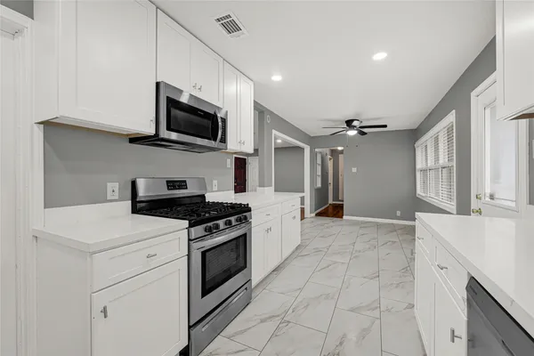 a kitchen with stainless steel appliances granite countertop grey cabinets a stove top oven a sink and dishwasher