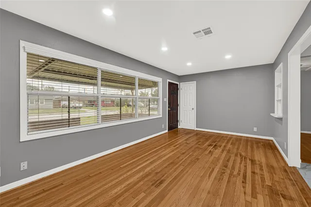 a view of an empty room with wooden floor and a window