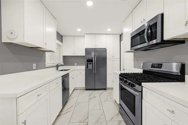 a kitchen with stainless steel appliances granite countertop a refrigerator stove a sink and dishwasher with white cabinets