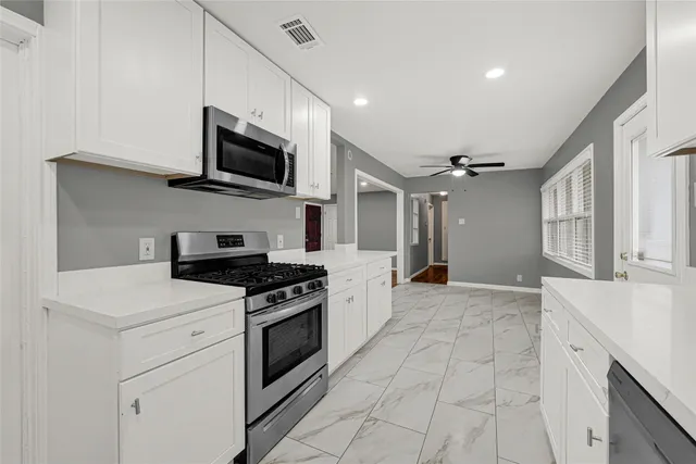 a kitchen with stainless steel appliances granite countertop grey cabinets a stove top oven a sink and dishwasher