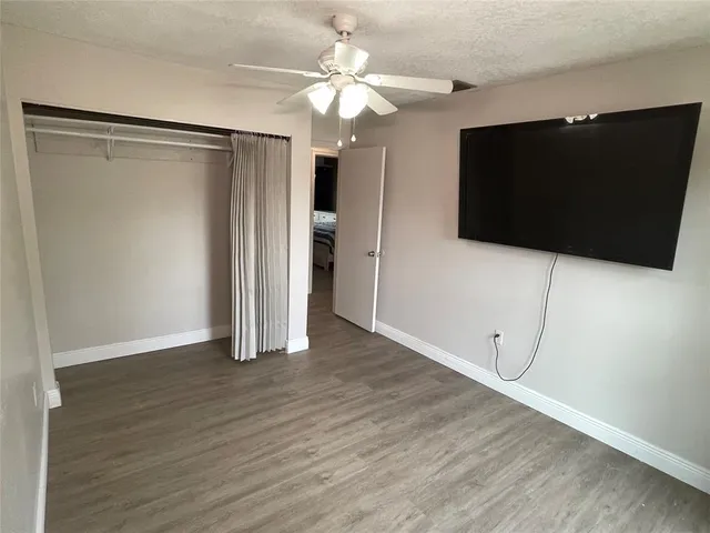 a view of an empty room with wooden floor and a ceiling fan
