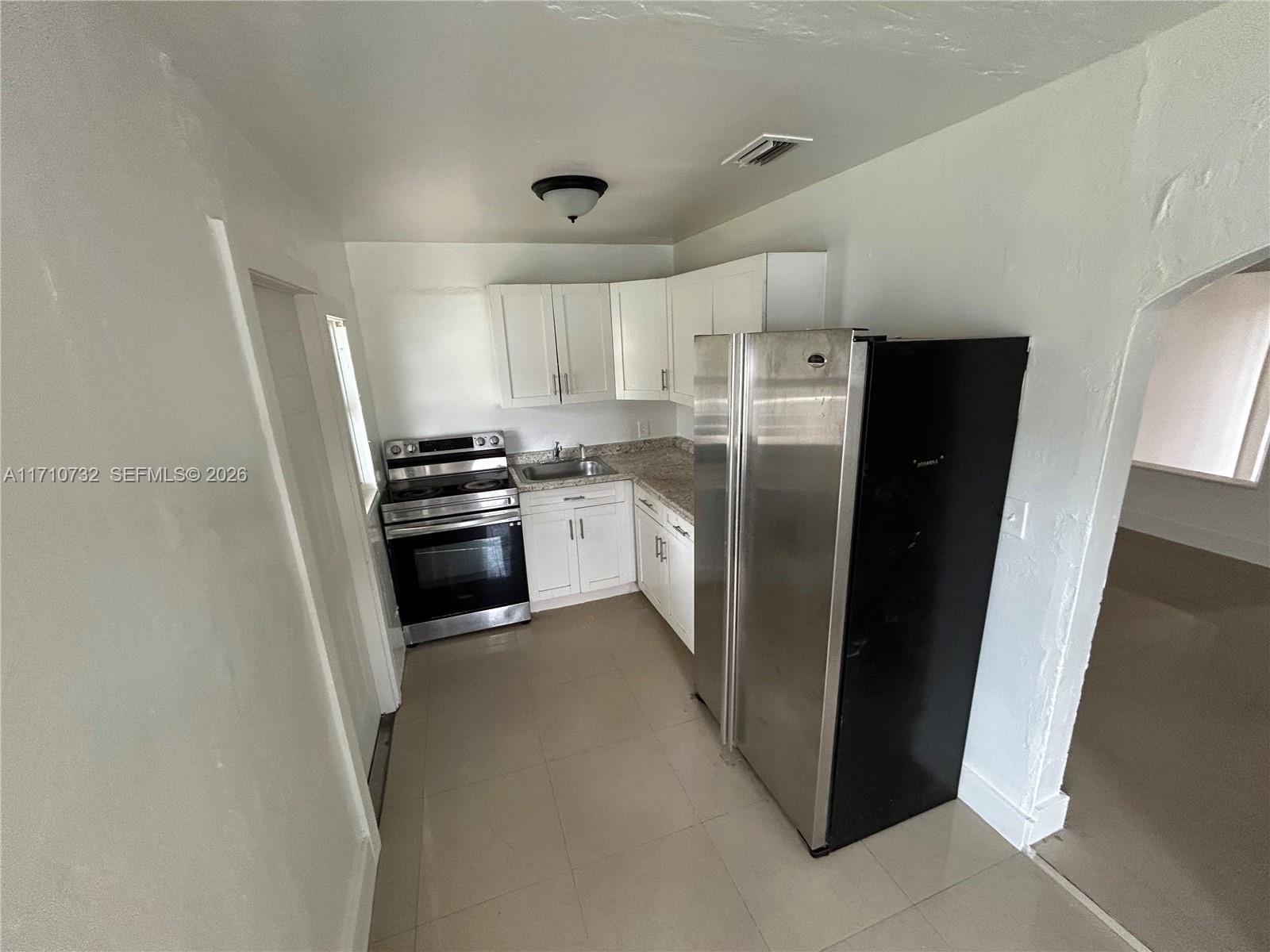 3529 Northwest 34th Street, Unit BACK Miami, FL 33142 - Photo 6 of 17 a kitchen with a refrigerator a stove top oven and white cabinets