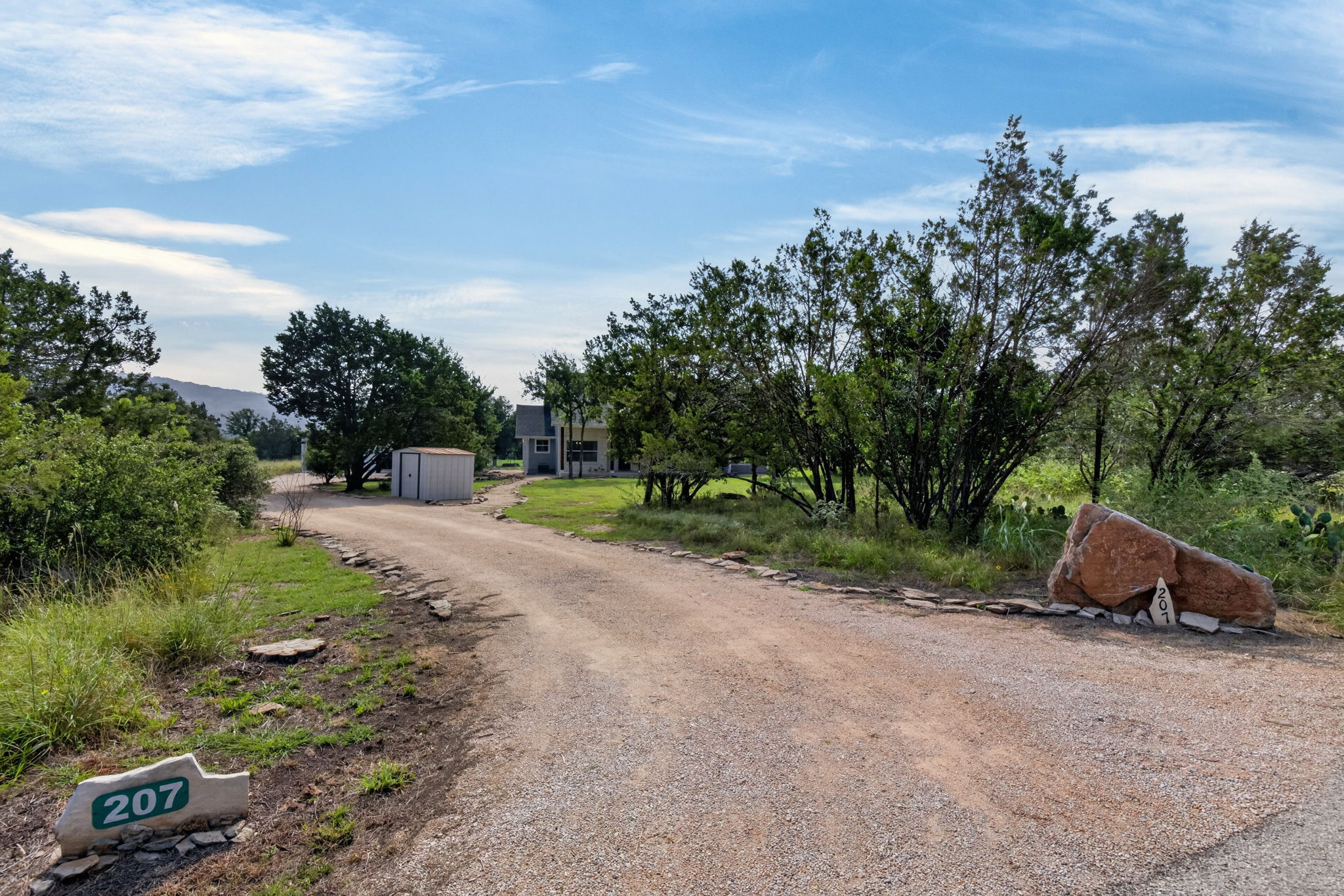 207 Deer Ridge Drive Burnet, TX 78611 - Photo 6 of 36 A long gravel driveway leads to a secluded house surrounded by mature trees and natural landscaping.