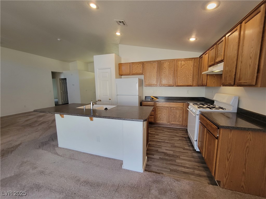 1112 Nevada Blaze Avenue North Las Vegas, NV 89081 - Photo 3 of 22 Kitchen with dark countertops, white appliances, vaulted ceiling, a kitchen island with sink, and brown cabinets
