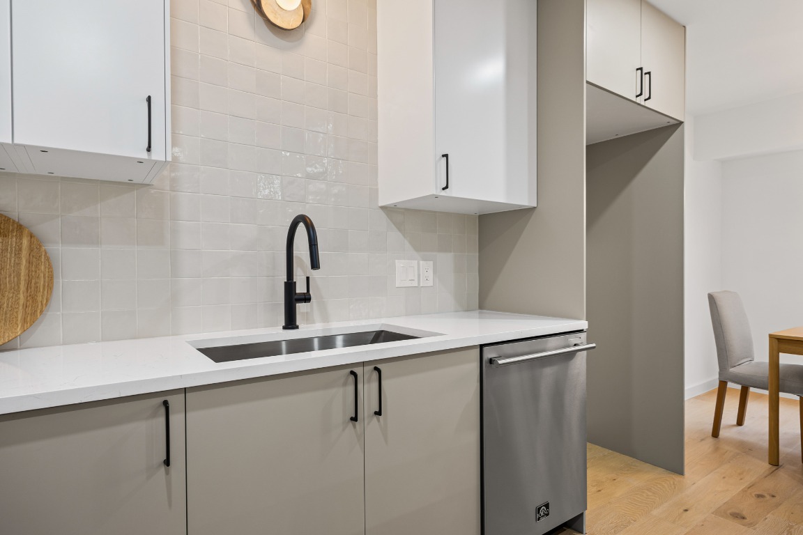 4609 Cliffstone Cove Austin, TX 78735 - Photo 10 of 33 Kitchen with stainless steel dishwasher, decorative backsplash, light stone counters, white cabinetry, and light wood-style flooring