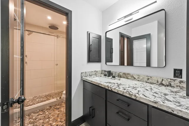 a bathroom with a granite countertop sink vanity mirror and shower