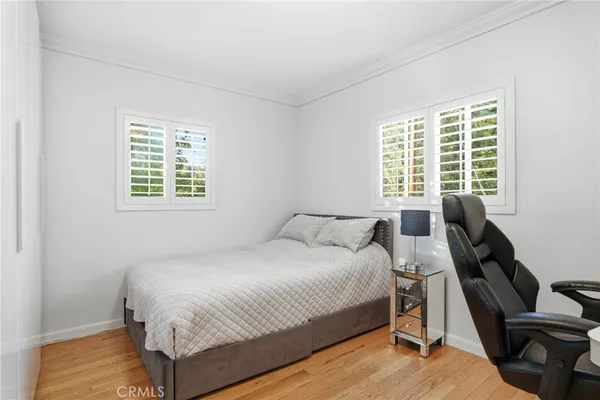 a bedroom with a bed a desk and chair with wooden floor next to a window
