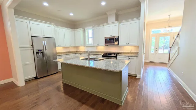 a kitchen with stainless steel appliances a stove a sink a refrigerator white cabinets and wooden floor