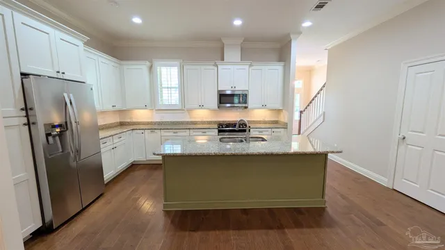 a kitchen with stainless steel appliances granite countertop a refrigerator a sink dishwasher a stove and white countertops with wooden floor