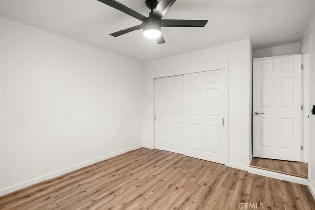 a view of an empty room with wooden floor and a ceiling fan