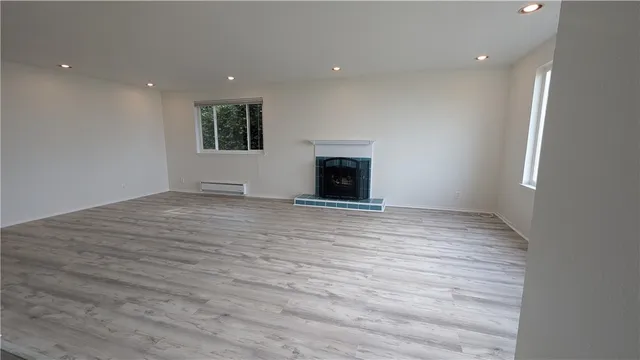an empty room with wooden floor fireplace and windows