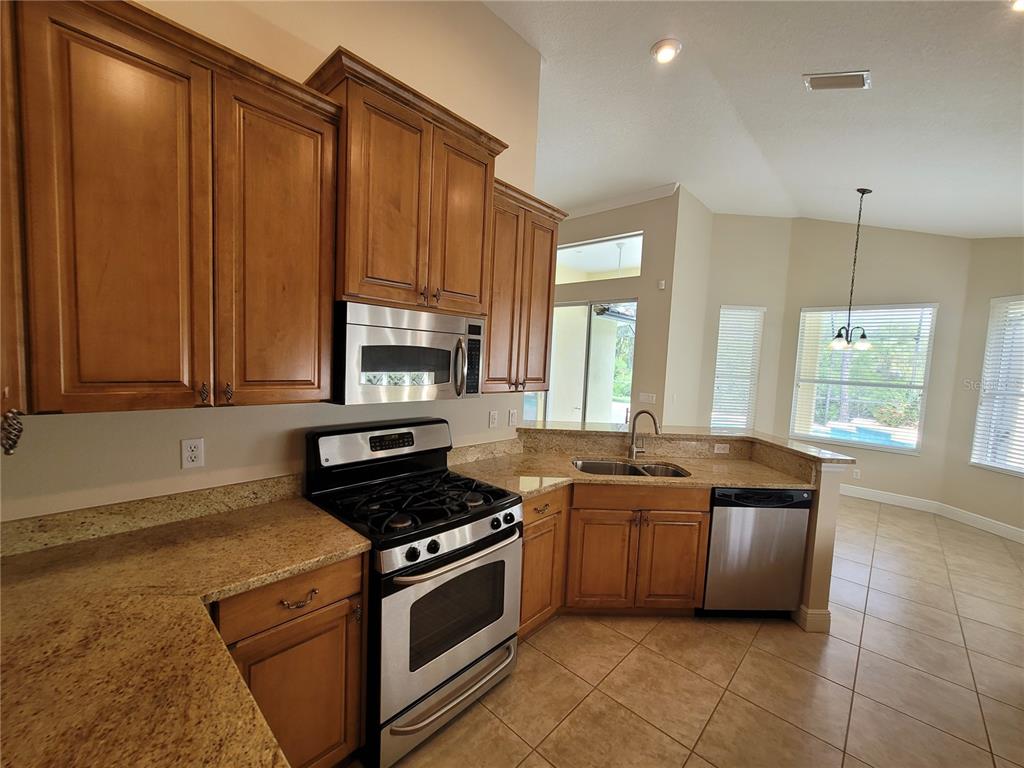 7486 Edenmore Street Lakewood Ranch, FL 34202 - Photo 16 of 28 a kitchen with stainless steel appliances granite countertop a stove a sink and a microwave