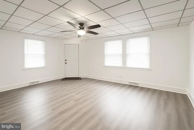 an empty room with wooden floor fan and windows