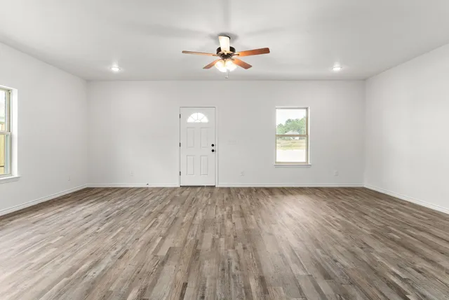 an empty room with wooden floor chandelier fan and windows