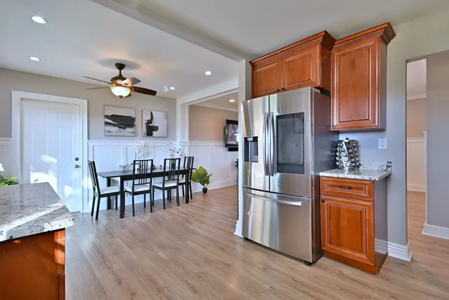 a kitchen with stainless steel appliances granite countertop a refrigerator a stove a sink a dining table and chairs with wooden floor