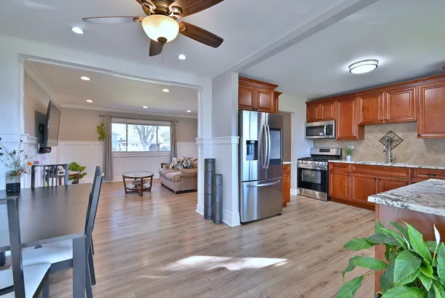 a kitchen with stainless steel appliances granite countertop a refrigerator a sink dishwasher a dining table and chairs with wooden floor