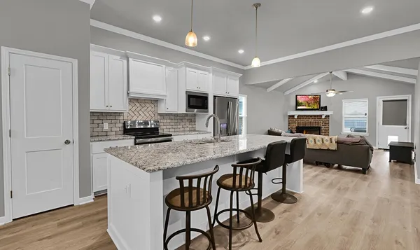 a kitchen with stainless steel appliances granite countertop a stove a refrigerator a sink a dining table and chairs with wooden floor