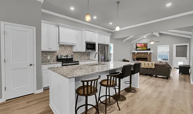 a kitchen with stainless steel appliances granite countertop a stove a refrigerator a sink a dining table and chairs with wooden floor