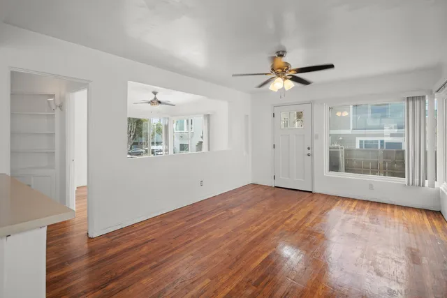 an empty room with wooden floor fan and windows