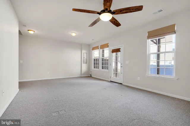 an empty room with chandelier fan and windows