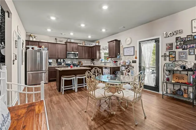 a kitchen with stainless steel appliances kitchen island granite countertop a refrigerator a stove a sink a dining table and chairs with wooden floor