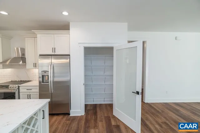 a large white kitchen with kitchen island a sink wooden floor and a refrigerator