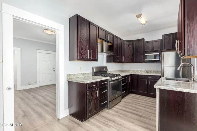 a kitchen with stainless steel appliances granite countertop a stove top oven a sink dishwasher and a refrigerator with wooden floor