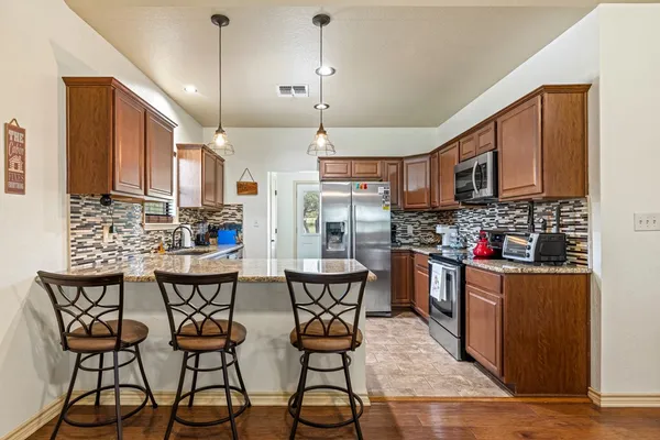 a kitchen with stainless steel appliances kitchen island granite countertop a table chairs and a refrigerator