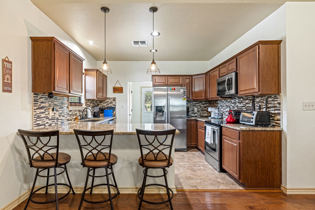 221 Coyote Trail Harper, TX 78631 - Photo 6 of 47 a kitchen with stainless steel appliances kitchen island granite countertop a table chairs and a refrigerator