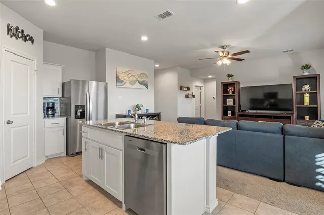 a kitchen with stainless steel appliances granite countertop a sink a refrigerator and a view of living room