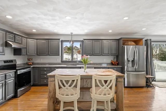 a kitchen with stainless steel appliances granite countertop a stove top oven a refrigerator a sink and chairs