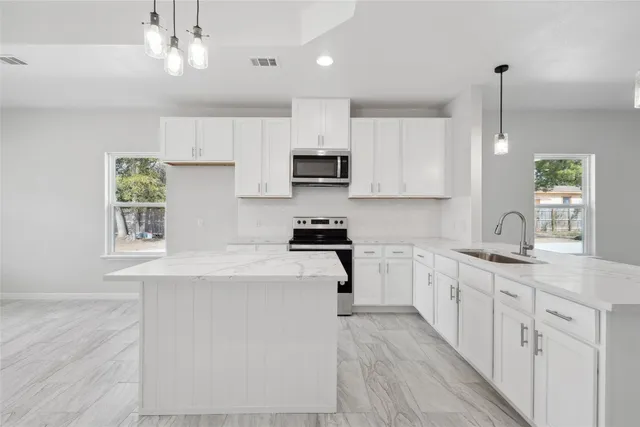 a large white kitchen with lots of counter space a sink appliances and cabinets