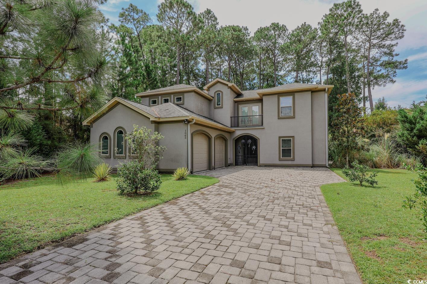 Mediterranean / spanish-style home with decorative driveway, an attached garage, stucco siding, a front yard, and view of scattered trees